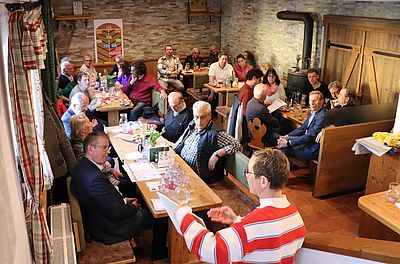 ca. 20 Personen, weiß, sitzen in Innneraum, eine Person erklärt etwas