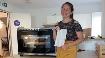 Junge Frau mit Brotsackerl, im Hintergrund ein Ofen zum Brot backen