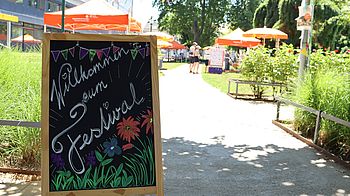 Aufsteller mit Schrift "Willkommen am Festival" und Blumen in Park