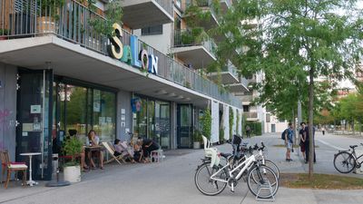 Ein Lokal im Erdgeschoss, davor sitzen Leute, Fahrräder parken daneben