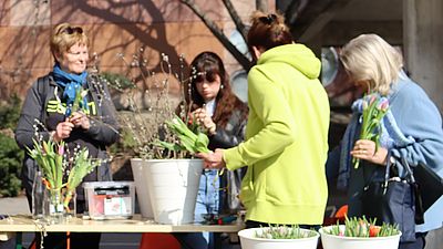 Mehrere Personen stehen im Freien um einen Tisch und binden Blumensträuße.