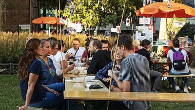 Menschen sitzen gemeinsam an einem Heurigentisch und unterhalten sich