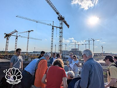 ca. 15 Personen stehen vor weiter Fläche mit vielen Kränen