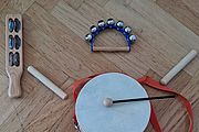 Set aus verschiedenen Holz-Musikinstrumenten für Kinder auf Parkettboden: Trommel mit Schlägel, zwei Maracas, ein Schellenstab, eine Schellentrommel und zwei Klanghölzer.