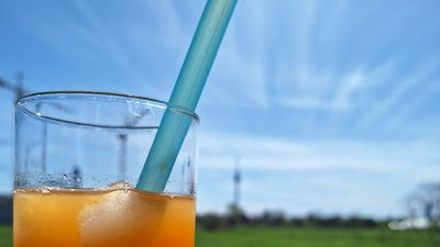 Ein Glas mit Saft und einem blauen Strohhalm. Im Hintergrund das Donaufeld.