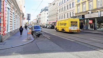 Blick entlang einer Straße gesäumt von Gründerzeithäusern. Am Straßenrand parkt ein gelber LKW mit der Aufschrift "Ottakringer"