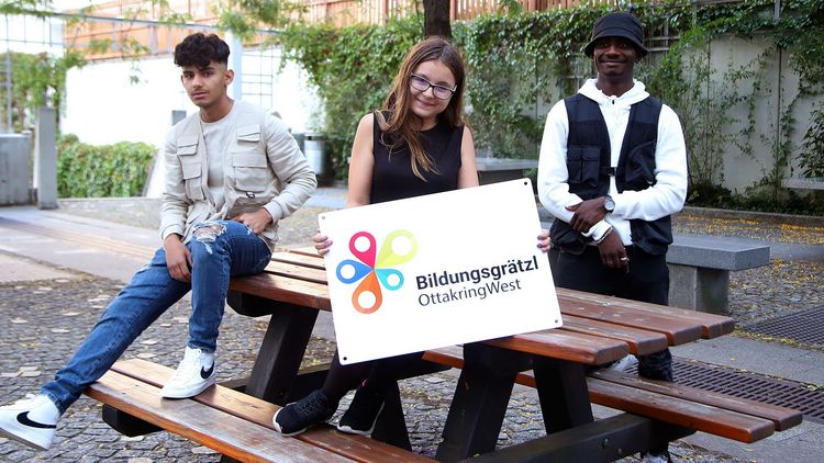 Bildungsgrätzl Drei SchülerInnen, die mittlere hält eine Tafel mit der Aufschrift "Bildungsgrätzl"