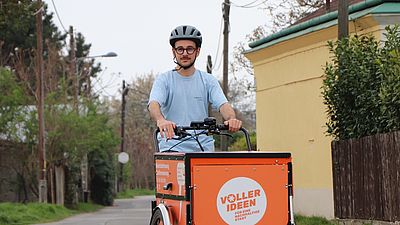 Eine Person fährt mit einem orangen Lastenrad auf einer Straße.