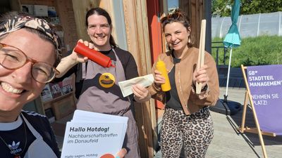 3 Personen lachen in die Kamera und halten einen Hotdog in die Höhe.