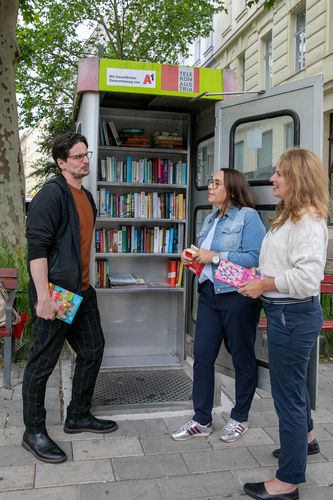 BV-StV Julia Lessacher, Karl Lampret und Annelies Larcher (GB*) stehen vor einer Bücherzelle.