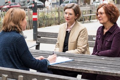 Straßeninterview zwei Personen werden von jemandem interviewt und sitzen gemeinsam am Tisch
