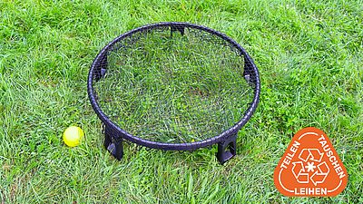 Ein Spikeball-Korb und ein gelber Spikeball liegen auf der grünen Wiese.