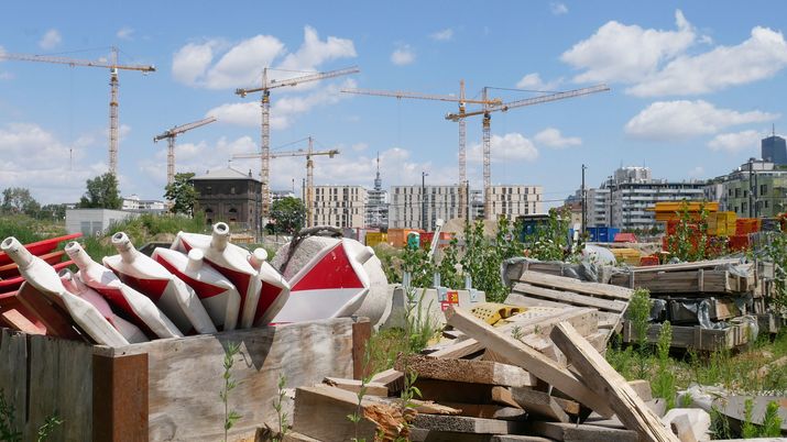 im Vordergrund einige Baustellen-Elemente und Materialien im Hintergrund einige Kräne