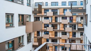 Aufnahme von einem der Wohngebäude. Es aht eine weiße Fassade und braune Gestaltungselemente um die Fenster und Balkone.