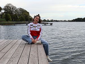 Eine junge Frau mit rot weißem Pullover und Jeans sitzt lässig an einem Badesteg an der Alten Donau.