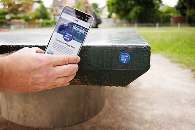 Eine Person hält ein Smartphone an einen Tischtennistisch und fotografiert einen QR-Code.