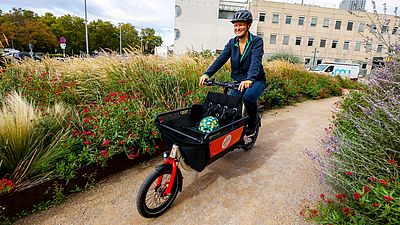Person fährt in Park auf Lastenfahrrad, das vorne Ladefläche hat