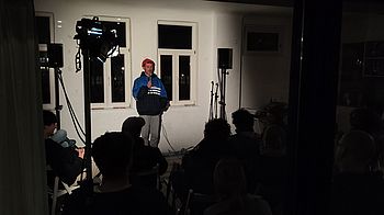 Person auf der Bühne ist hell angestrahlt, restlicher Raum dunkel