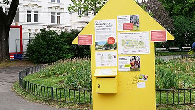 Ausstellungstafel in Form eines gelben Pfeils der nach oben zeigt in einem Park