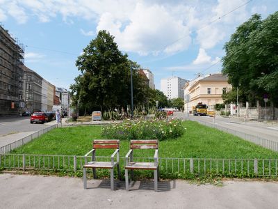 Grünfläche umgeben von Straßen, davor zwei Stühle