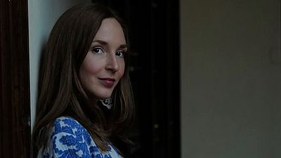 Frau mit langen Haaren lehnt leicht lächelnd an Wand