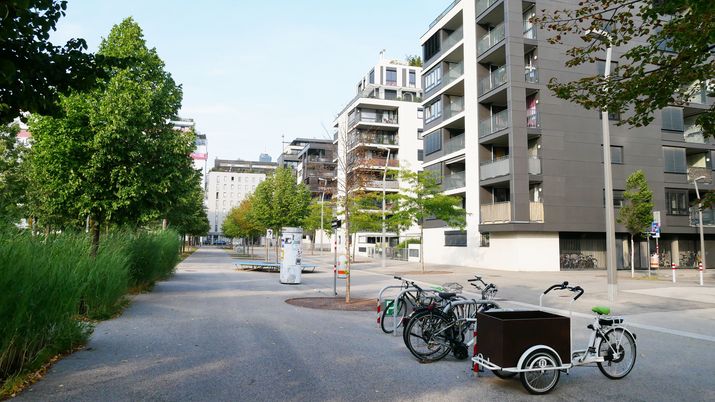 Neue Wohngebäude, ein Autofreier Weg und ein grüner Park, im Vordergrund parkt ein Lastenfahrrad