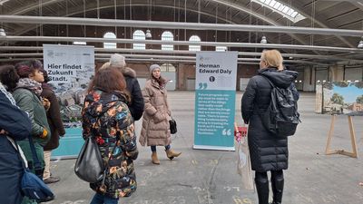 Warm in winterliches Gewand eingepackte Menschengruppe, die in einer Backsteinhalle vor Ausstellungsdisplays stehen.