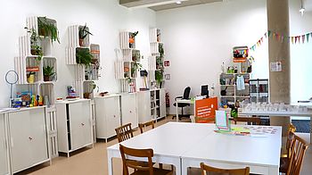 Innenraum mit Tisch, Sessel, Kästen und Pflanzen an der Wand