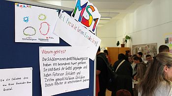 Eingangsschild der Ausstellung "Sprachen in Bildern" und Personen im Hintergrund.