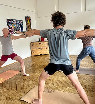 drei Personen in Innenraum amchen Yogaübung stehend