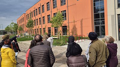 Eine Gruppe von Menschen Blicken auf die Fassade eines Gebäudes, dort sind Nistkästen für Vögel und Fledermäuse eingebaut