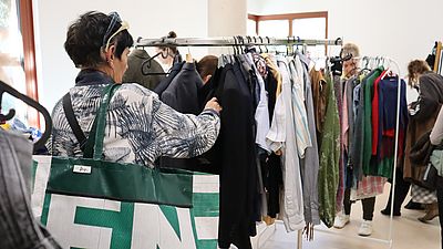 Eine Frau stöbert beim Kleidertausch durch Kleidungsstücken auf Stangen