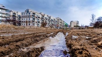 Das Wasser in den Erdabdrücken von Reifen der Baufahrzeuge ist gefroren. Im Hintergrund befinden sich fertige Wohnhäuser.