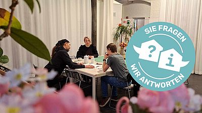 Drei Personen sitzen redend an einem großem, weißen Tisch.