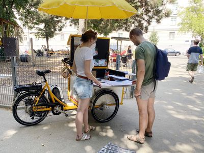 Zwei Personenstehen bei einem lastenrad mit gelbem Sonnenschirm und reden