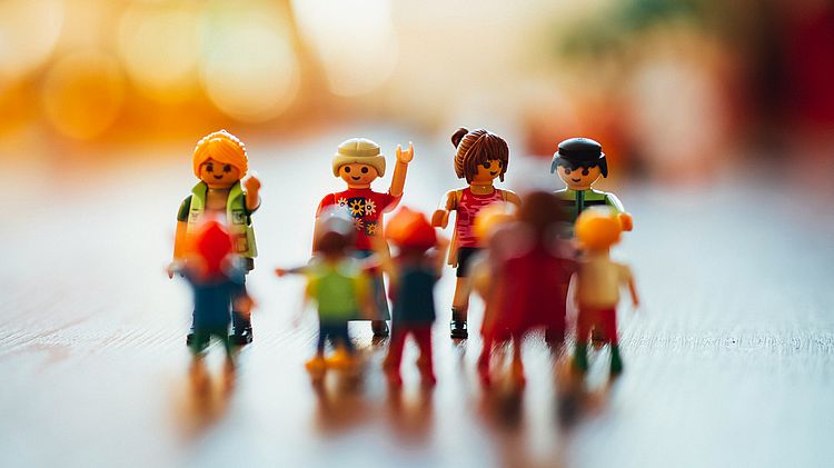 Playmobilfiguren in unetrschiedlichen Ausführungen und Größen wirken wie eine im Kreis stehende, gestikulierende und im Gespräch vertiefte Menschengruppe.