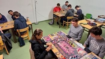 In einem Gemeinschaftsraum sitzen um 3 Tische mehrere Menschen und Spielen Brettspiele miteinander.