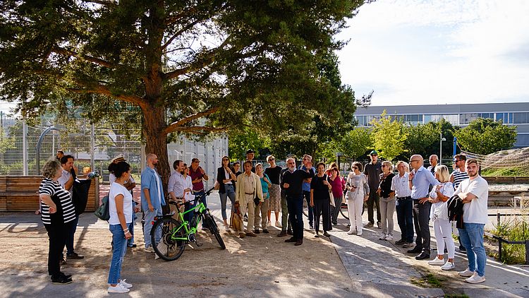 Eine Gruppe von Menschen versammelt sich unter einem Baum - anlässlich einer geführten Stadtteiltour der GB*