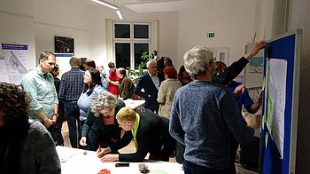 Menschen zeigen auf Pläne und schreiben etwas auf bunte Post-Its