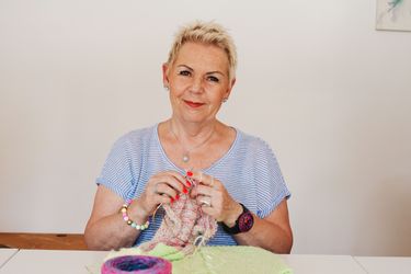 Michaela Mraz strickt an ihrem nächsten Werk. Vor ihr liegt eine rosa Wolle.