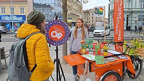 Eine Person steht hinter einem Infostand in Form eines Lastenrads, während sich eine andere Person informiert.