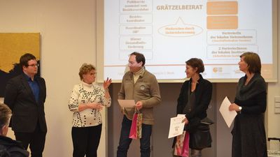 6 Personen stehen vor einer Powerpointpräsentation und diskutieren