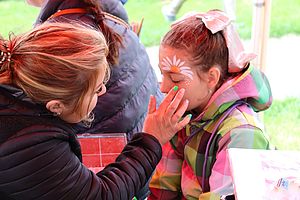 eine Person schminkt ein Kind im Gesicht mit Blumen