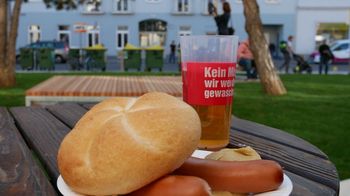 Ein Paar Frankfurter mit Semmel auf einem runden Pappteller steht auf einem Tisch im Freien