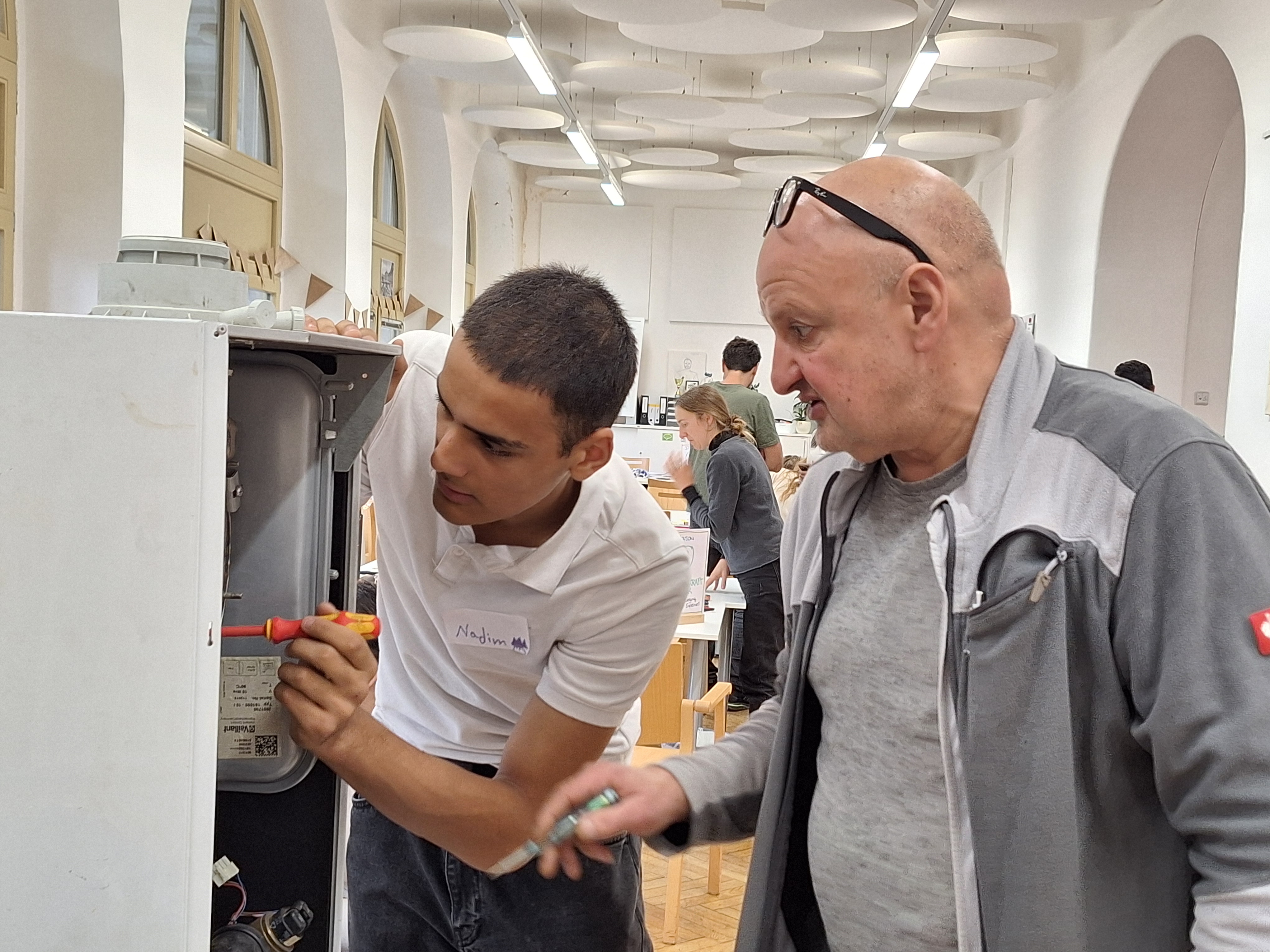 Zwei Personen, männlich gelesen, jung und alt, schrauben an etwas herum.