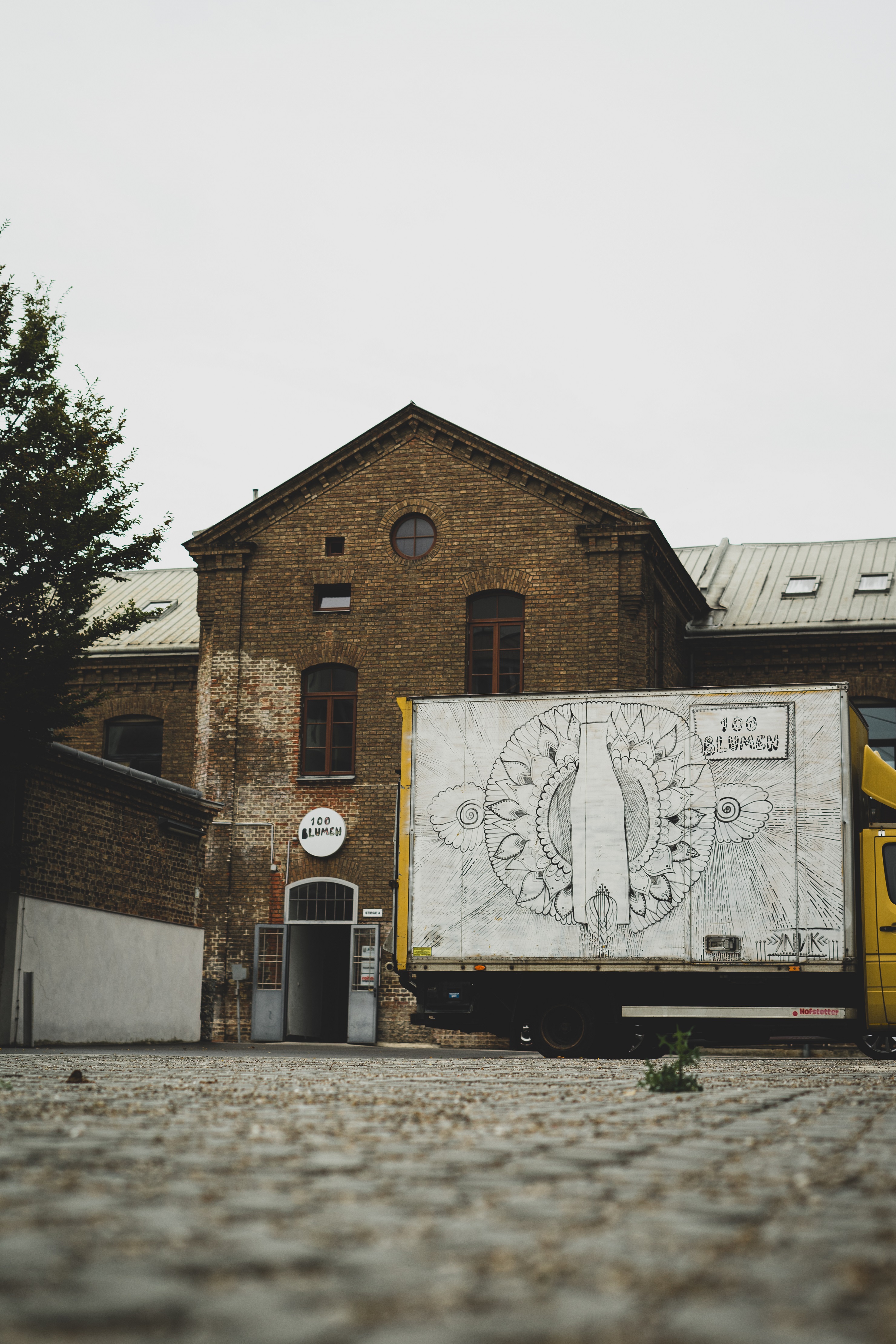 Schwarz-weißer LKW vor altem Backsteinhaus mit Aufschrift "100 Blumen"